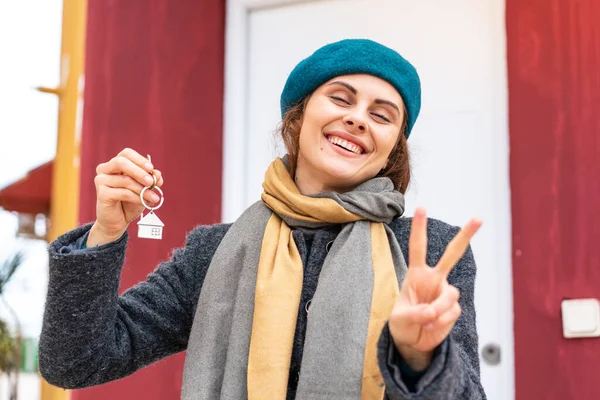 布鲁内特女人微笑着拿着家里的钥匙 展示胜利的标志 — 图库照片