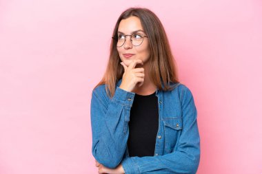 Pembe arka planda izole edilmiş genç beyaz kadın yukarı bakarken bir fikir düşünüyor.