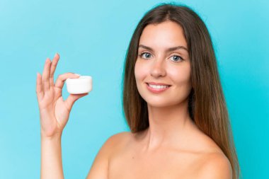 Genç beyaz kadın, mavi arka planda nemlendirici ile izole edilmiş.