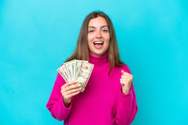 Kafkasyalı genç bir kadın mavi arka planda izole edilmiş bir şekilde çok para alıyor. Kazanan pozisyondaki zaferi kutluyorlar.