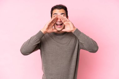 Pembe arka planda izole edilmiş genç beyaz adam bağırıyor ve bir şey duyuruyor.