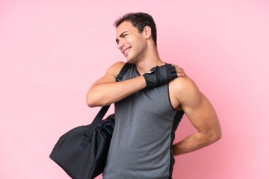 Spor çantalı beyaz bir genç, pembe arka planda izole edilmiş. Omuz ağrısı çekiyor. Çabaladığı için.