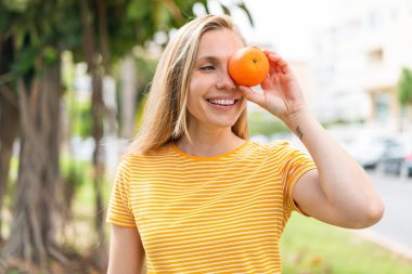 Açık havada elinde portakal tutan genç sarışın kadın.