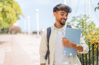 Genç bir Arap öğrenci açık havada neşeli bir ifadeyle.