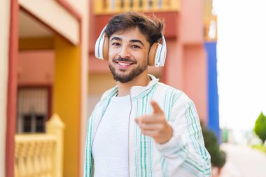 Yakışıklı bir Arap açık havada müzik dinliyor ve ön tarafı işaret ediyor.