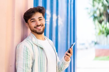 Yakışıklı bir Arap açık havada cep telefonu kullanıyor ve gülümsüyor.