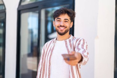 Dışarıdaki yakışıklı bir Arap, elinde mutlu bir ifadeyle cüzdan tutuyor.