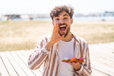 Yakışıklı bir Arap açık havada sashimi tutuyor ve ağzı açık bağırıyor.