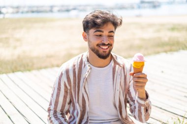 Açık havada kornet dondurmalı yakışıklı bir Arap, neşeli bir ifadeyle.