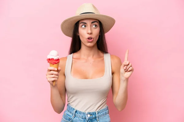 年轻的高加索女人 拿着用粉红背景隔开的玉米粒冰淇淋 想着用手指指指一下 — 图库照片