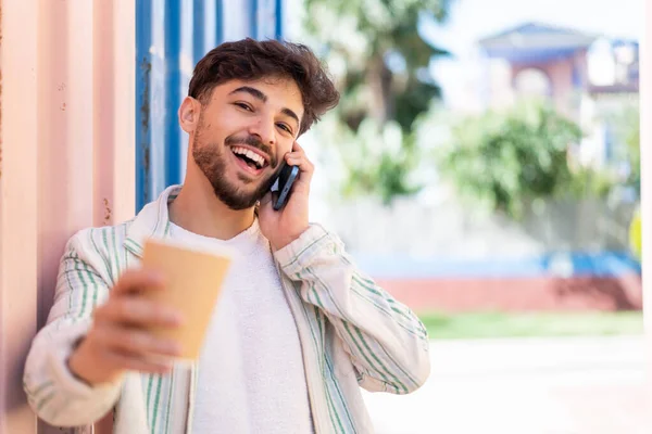 Fešák Arab Muž Venku Pomocí Mobilního Telefonu Drží Kávu Veselým — Stock fotografie