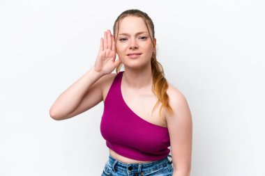 Beyaz arka planda izole edilmiş genç beyaz kız elini kulağına koyarak bir şeyler dinliyor.