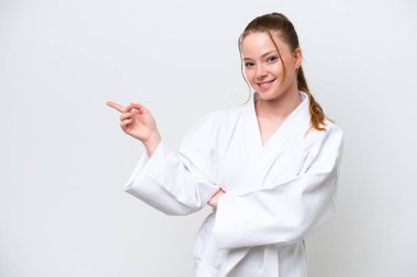 Beyaz arka planda karate yapan beyaz tenli genç bir kız parmak işareti yapıyor.