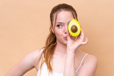 Beyazlı genç bir kız elinde avokado tutarak bej arka planda izole edilmiş. Portreyi kapat
