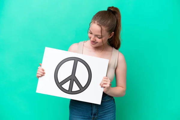 緑の背景に隔離された若い白人女性平和のシンボルを持つプラカードを保持 — ストック写真