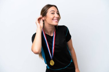 Young caucasian woman with medals isolated on white background listening to something by putting hand on the ear