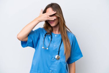 Mavi arka planda izole edilmiş genç bir cerrah kadın. Gözleri elleriyle kaplıyor ve gülümsüyor.