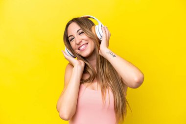 Sarı arka planda izole edilmiş genç beyaz kadın müzik dinliyor.