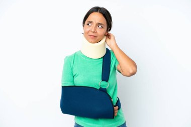 Young hispanic woman wearing a neck brace and sling isolated on white background having doubts