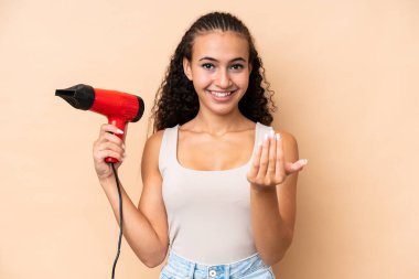 Elinde bej arka planda izole edilmiş bir saç kurutma makinesi tutan genç bir kadın, bizimle gelmesi için davet ediyor. Gelmene sevindim.