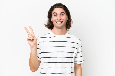 Beyaz arka planda izole edilmiş yakışıklı genç adam gülümsüyor ve zafer işareti gösteriyor