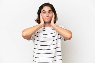 Beyaz arka planda izole edilmiş genç yakışıklı adam hayal kırıklığına uğramış ve kulaklarını kapatmış.