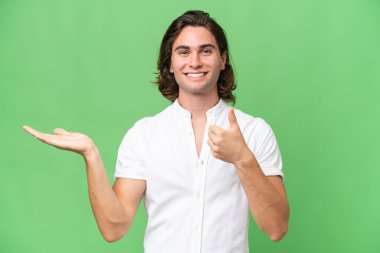 Kafkasyalı genç adam yeşil krom arka planda izole edilmiş. Kopyalama alanı hayali bir şekilde avucunun içinde duruyor. Bir ilan vermek için.