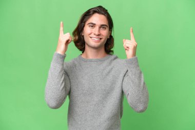 Genç beyaz adam yeşil krom arka planda izole edilmiş. Harika bir fikre işaret ediyor.