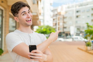 Genç yakışıklı adam cep telefonu kullanıyor ve geriye doğru işaret ediyor.