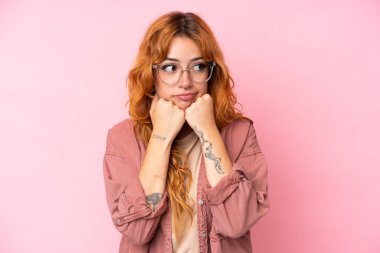 Pembe arka planda gözlüklü ve yorgun genç beyaz kadın.