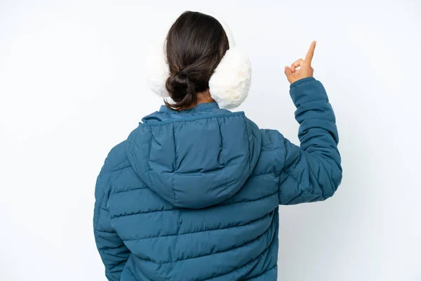 年轻的惊慌失措的女人戴着冬季的耳罩 背景是白色的 食指指向后方 — 图库照片