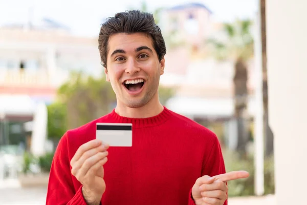 Young Handsome Man Holding Credit Card Outdoors Surprised Pointing Finger — Stock Photo, Image