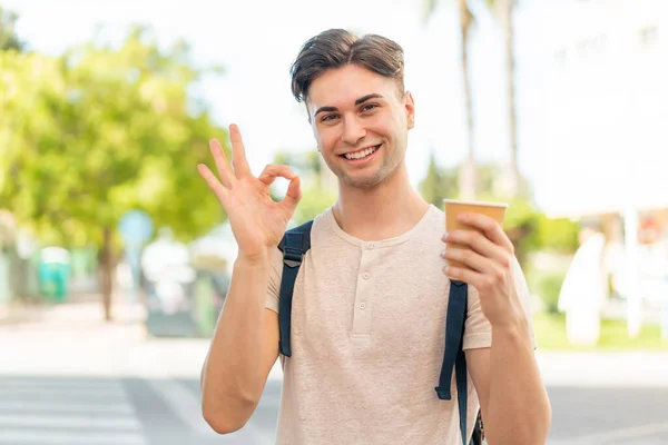 Mladý Pohledný Muž Drží Odnést Kávu Venku Ukazuje Znamení Prsty — Stock fotografie