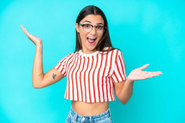 Yüzünde şok ifadesi olan mavi arka planda izole edilmiş beyaz bir kadın.