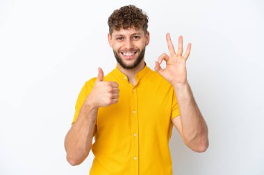 Beyaz arka planda izole edilmiş yakışıklı beyaz bir adam tamam işareti ve baş parmak hareketi gösteriyor.