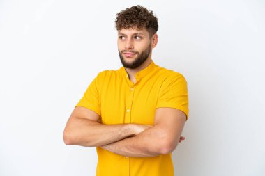 Beyaz arka planda izole edilmiş yakışıklı beyaz bir adam omuzlarını kaldırırken şüpheyle hareket ediyor.