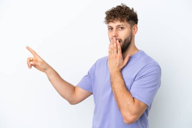 Beyaz arka planda izole edilmiş yakışıklı beyaz bir adam sürpriz bir ifadeyle işaret ederken...