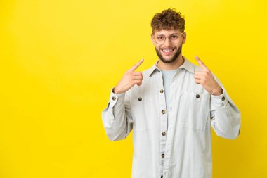Sarı arka planda izole edilmiş yakışıklı beyaz bir adam baş parmak işareti yapıyor.