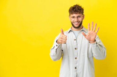 Sarı arka planda izole edilmiş yakışıklı beyaz adam parmakları olan altı kişi sayıyor.