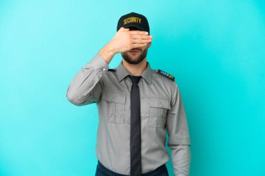 Genç güvenlik görevlisi mavi arka planda tek başına, gözleri elle kapatıyor. Bir şey görmek istemiyorum.