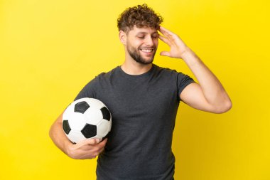 Yakışıklı genç futbolcu. Sarı arka planda izole edilmiş. Çok gülümsüyor.