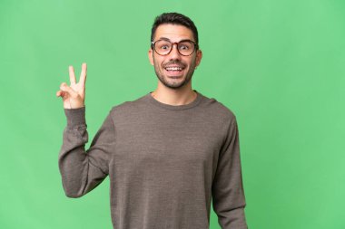 Genç, yakışıklı, beyaz bir adam izole edilmiş arka planda gülümsüyor ve zafer işareti gösteriyor.