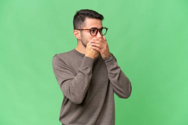 Genç, yakışıklı, beyaz bir adam izole edilmiş arka planda ağzını kapatıyor ve yan tarafa bakıyor.