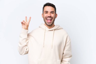 Beyaz arka planda izole edilmiş genç beyaz adam gülümsüyor ve zafer işareti gösteriyor.