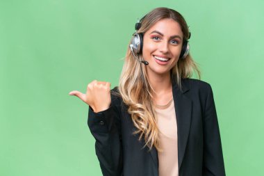 Tele pazarlamacı güzel Uruguaylı kadın tecrit edilmiş arka planda çalışan bir kulaklıkla bir ürünü sunmak için kenarı işaret ediyor.