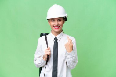 Young architect woman with helmet and holding blueprints over isolated background giving a thumbs up gesture