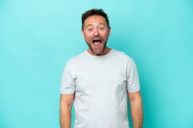 Orta yaşlı beyaz bir adam mavi arka planda izole edilmiş ve yüzünde sürpriz bir ifade var.