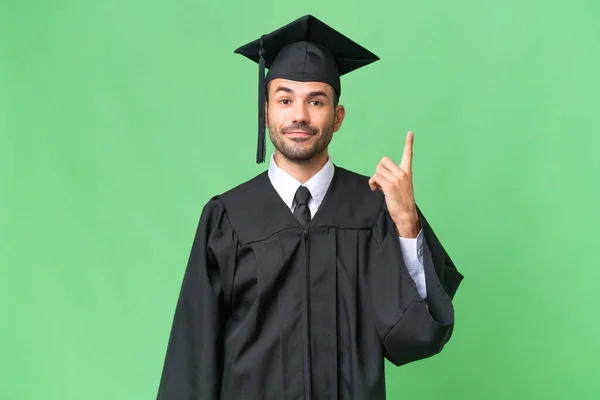 Mladý Vysokoškolský Absolvent Muž Přes Izolované Pozadí Ukazuje Ukazováčkem Skvělý — Stock fotografie