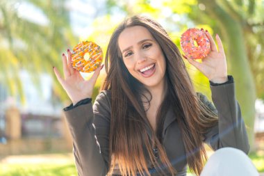 Açık havada elinde mutlu bir ifadeyle donut tutan genç bir kadın.