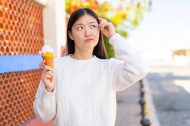 Açık havada kornet dondurması olan güzel Çinli bir kadın. Şüpheleri var ve kafası karışmış bir yüz ifadesi var.